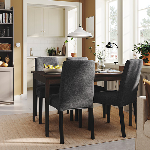 Comedor con sillas oscuras alrededor de mesa de madera, cuenco de frutas. Cocina con armarios blancos, bien iluminada, acogedora.