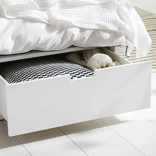 Cama blanca con cajón de almacenamiento abierto, ropa de cama blanca y blanca, suéter de punto blanco en el interior, bajo una luz brillante.