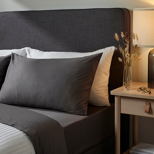 NATTJASMIN funda de almohada gris oscuro y ropa de cama puesta en cama, con mesita de noche de madera y jarrón.