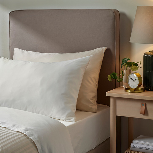 Fundas de almohada blancas NATTJASMIN sobre cama con cabecero y mesita de noche grises.