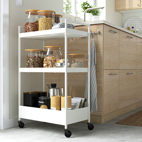 Pequeño carro de almacenamiento blanco de ikea NISSAFORS con múltiples estantes, que contienen varios artículos de cocina. Cabe en espacios reducidos, sobre ruedas para mayor movilidad.