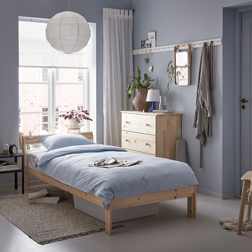 Dormitorio minimalista con paredes celestes, cama de madera clara NEIDEN, ropa de cama azul, lámpara colgante blanca, tocador de madera, cortinas grises y alfombra estampada.