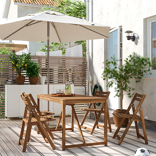 Patio de madera con sombrilla en cubierta. Cuatro sillas, plantas y casa al fondo.