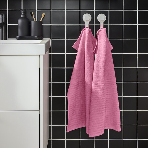 Las toallas VÅGSJÖN rosas cuelgan de ganchos junto a una pared de azulejos oscuros con un lavabo blanco.