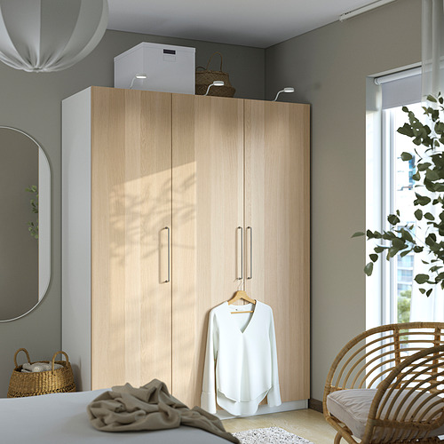 Armario PAX: armario alto en tono madera con espejos y camisa colgante. Al lado de la silla y la planta de mimbre.