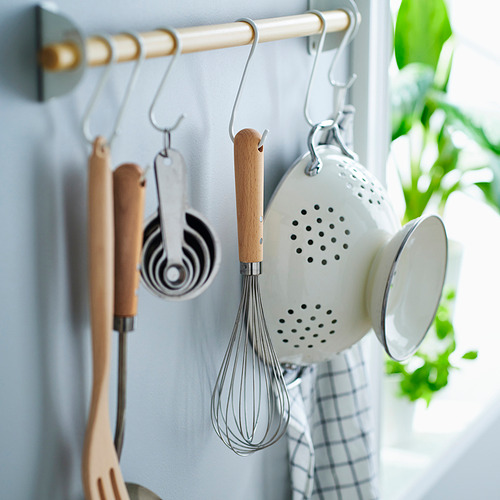 Barandilla de cocina con ganchos que sujetan utensilios, batidor, tazas medidoras y un colador. Plante a la derecha.