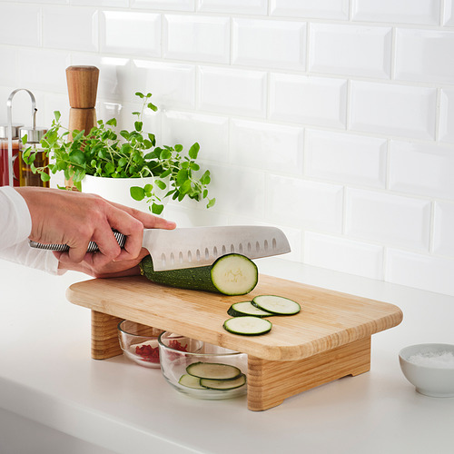 Persona cortando pepino en una tabla de cortar de madera con ranuras para atrapar rodajas.
