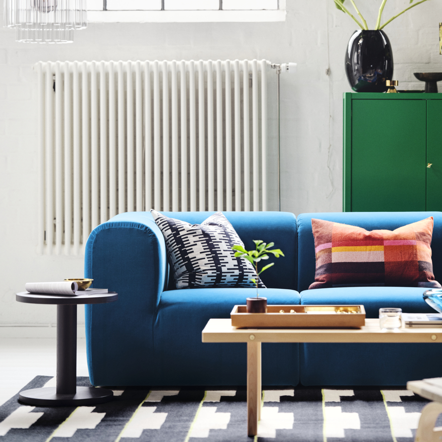 Sofá azul, decoración colorida, alfombra geométrica, radiador blanco, armario verde.