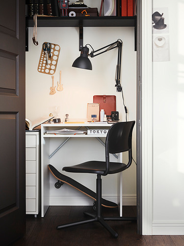 Oficina en casa compacta: escritorio blanco, silla negra, lámpara de pared, monopatín, decoración de guitarra.