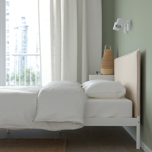 Dormitorio con cama KLEPPSTAD, estructura de metal blanco, cabecero textil y lámpara de cesta tejida en cabecero. Gran ventanal con vista a la ciudad.