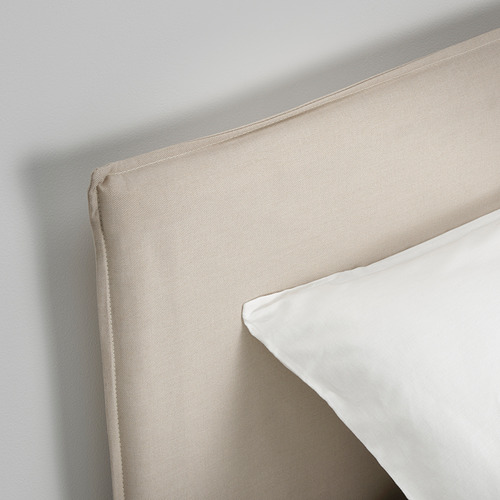 Un primer plano de una cama moderna, cabecero y almohada. Tejido beige claro, diseño elegante, borde cuidadosamente cosido.