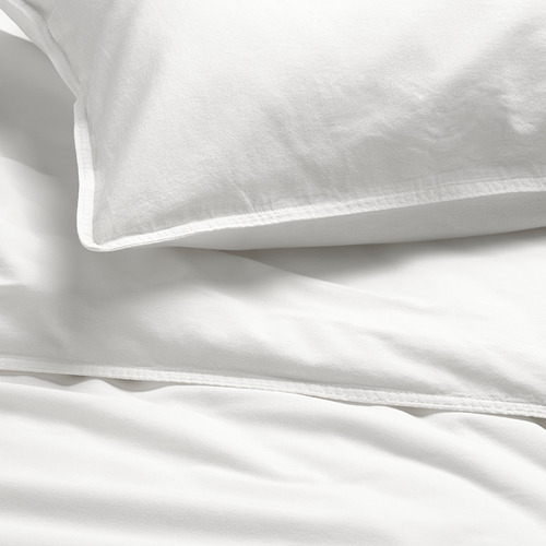 Una cama acogedora con edredón y sábanas de algodón blanco, suave, de alta calidad y liso. La luz del sol proyecta sombras suaves sobre la ropa de cama, resaltando su textura.