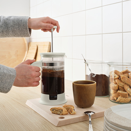 Persona presionando el émbolo en una cafetera / tetera UPPHETTA en el mostrador de la cocina, con café y galletas cerca.