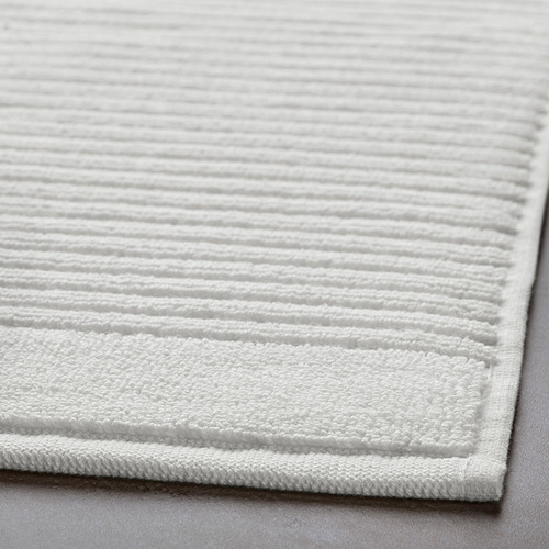 Primer plano de una alfombra de baño de algodón blanco afelpada con una textura intrincada, que muestra su material suave y absorbente.