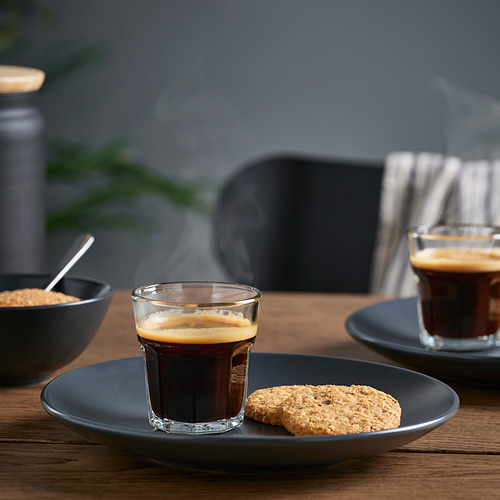 Dos vasos pequeños de espresso humeante en platos con galletas al lado.