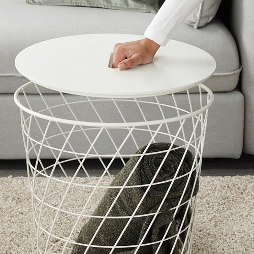 Una persona levantando una mesa blanca de KVISTBRO con una cesta, mostrando su diseño ligero y fácil de mover.