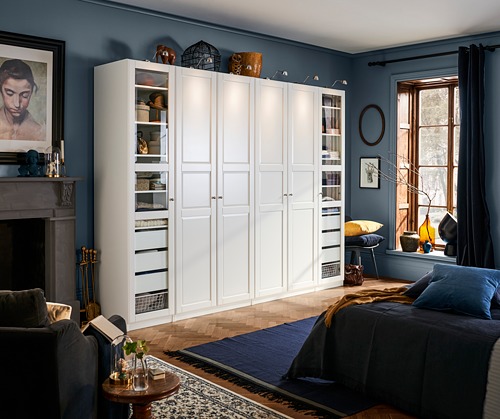 Gran armario blanco TYSSEDAL con paneles de cristal que muestra la decoración. Paredes azules y muebles oscuros en una habitación acogedora.