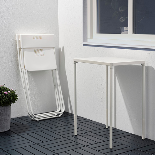 Una silla plegable de metal blanco se apoya en una pared blanca junto a una pequeña mesa blanca sobre una cubierta de madera.