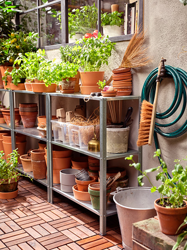 Almacenamiento de plantas al aire libre: estantería HYLLIS de acero galvanizado que contiene macetas de terracota, herramientas de jardinería y plantas. Manguera verde y cepillo adjuntos.