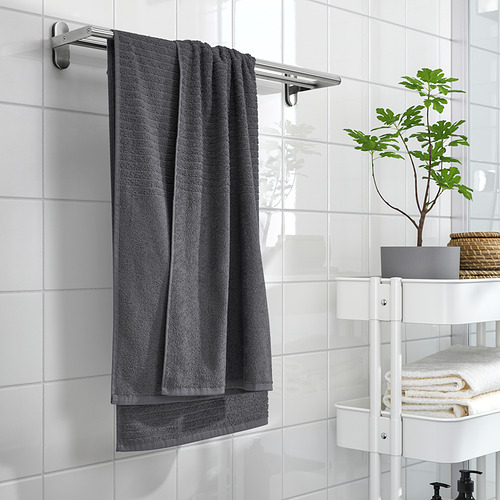 Baño moderno con toallas VÅGSJÖN grises, azulejos blancos y una planta verde.