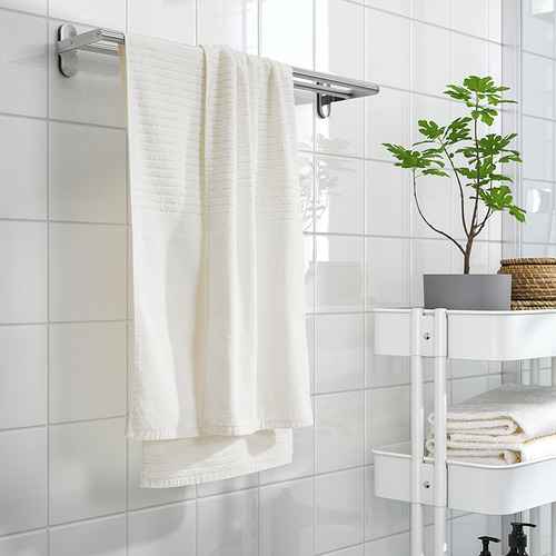 Toalla blanca sobre perchero con rayas, se pliega cuidadosamente. Pequeña planta en maceta, toallas y estanterías en un baño limpio y minimalista.