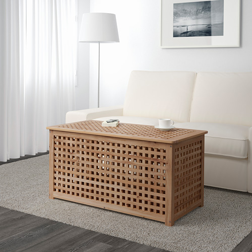 La mesa de centro de celosía de madera con almacenamiento se encuentra cerca de un sofá blanco. Tiene capacidad para una taza y un control remoto, lo que ofrece un práctico espacio de almacenamiento.