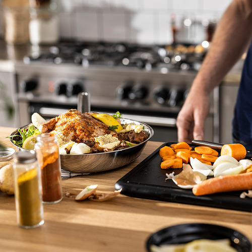 Mostrador de madera con alimentos cocinados, verduras preparadas y rallador; horno borroso.