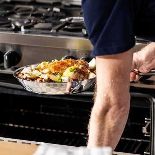 Persona que sostiene una sartén de vidrio con pollo cocido y verduras, colocándola en un horno.