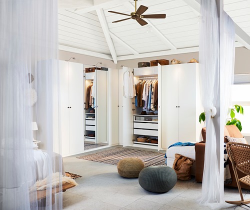Dormitorio amplio y luminoso con armario con puerta FORSAND blanca, ropa tendida, pufs, planta y silla de mimbre.