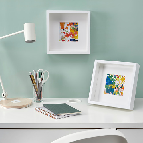 Un escritorio bien iluminado con coloridas obras de arte enmarcadas, una lámpara, artículos de papelería y blocs de notas, que muestran una configuración de espacio de trabajo útil y estéticamente agradable.