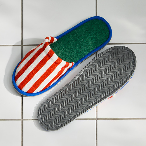 Dos zapatillas de rayas de colores en el suelo de baldosas, con la suela hacia arriba, con agarres antideslizantes estampados.