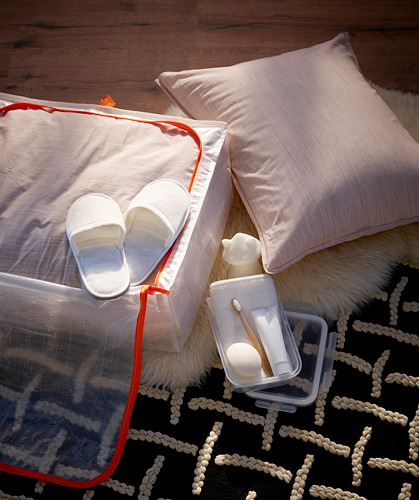 Cama con estuche rojo PÄRKLA, zapatillas blancas, artículos de tocador. Piso rústico.