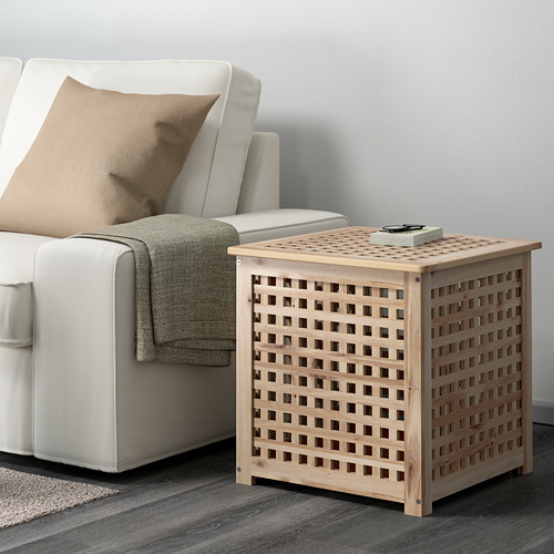 Junto a un sofá blanco se encuentra una mesa auxiliar de madera HOL con diseño de celosía, que destaca por su pequeño tamaño y su práctico almacenaje.