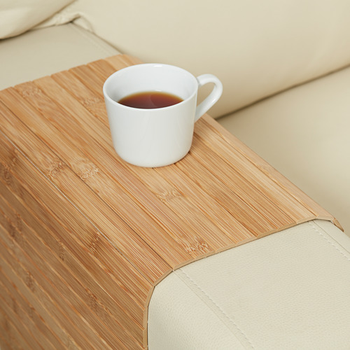 Una bandeja de bambú sostiene una taza de café sobre un sofá beige.