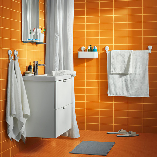 Baño con azulejos de color naranja brillante con accesorios blancos. Incluye tocador blanco, espejo, toallas, pantuflas y una alfombra de baño gris.