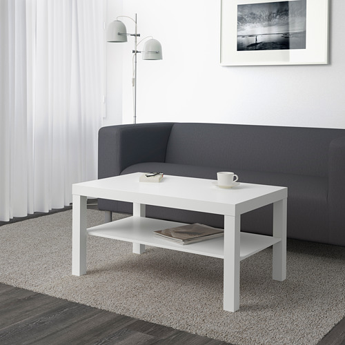 Sala de estar moderna con una elegante mesa de café blanca LACK frente a un sofá gris, con una taza y una pila de libros.
