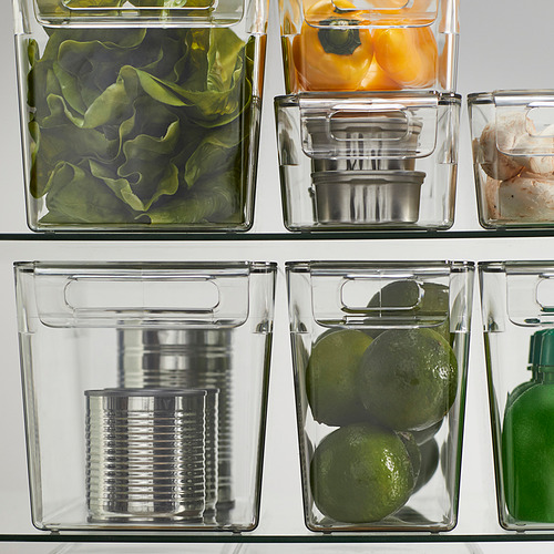 Cajas de almacenamiento de plástico transparente para refrigerador con tapa, que contienen frutas, verduras y latas, apilables para ahorrar espacio.