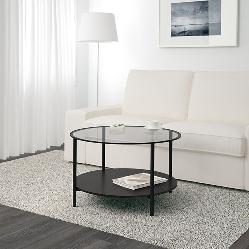 Sala de estar moderna con un elegante sofá blanco y una mesa de centro VITTSJÖ con tapa de vidrio que sostiene una taza, un platillo, un control remoto y una revista.