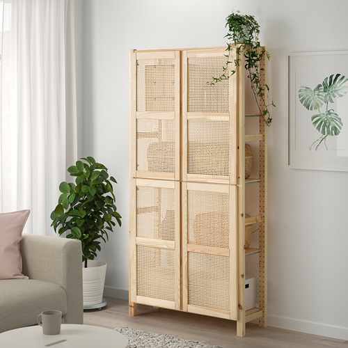 Estantería IVAR con puertas de bambú, pino, de pie junto a plantas y sofá gris.