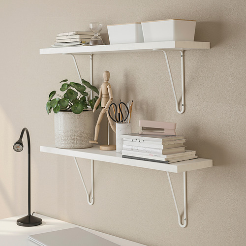 Estanterías blancas montadas en la pared con libros, macetas y artículos decorativos, con una lámpara de escritorio negra.