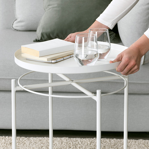 La persona coloca las copas de vino en la mesa auxiliar GAZOM. Bandeja redonda moderna, blanca, sobre base metálica. Diseño simple y conveniente para servir.