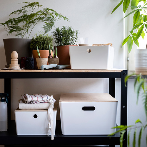 Estantería con cajas blancas KUGGIS, tapas de bambú, plantas y telas; Las cajas almacenan los artículos de forma ordenada.