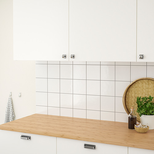 Cocina moderna con encimera de bambú, armarios blancos, cuenco, jarrón, botella.