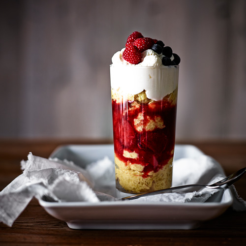 Taza de postre de vidrio alta llena de capas de pastel, crema y bayas; Perfecto para dulces.