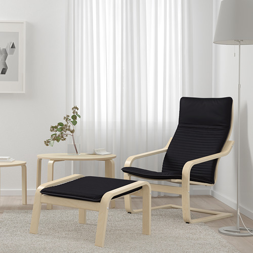 Silla y otomana acolchadas negras en habitación minimalista con mesa de flores.