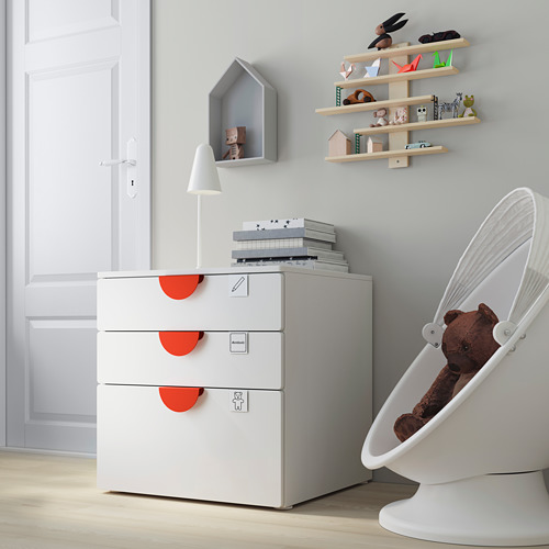 Moderna habitación para niños con un cofre SMÅSTAD blanco, estantes de madera clara y una silla colgante blanca con un oso de peluche.