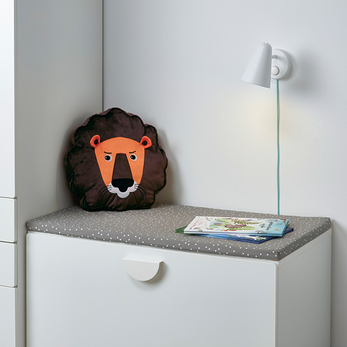 Suave almohada de león, libro y lámpara sobre mesa acolchada.