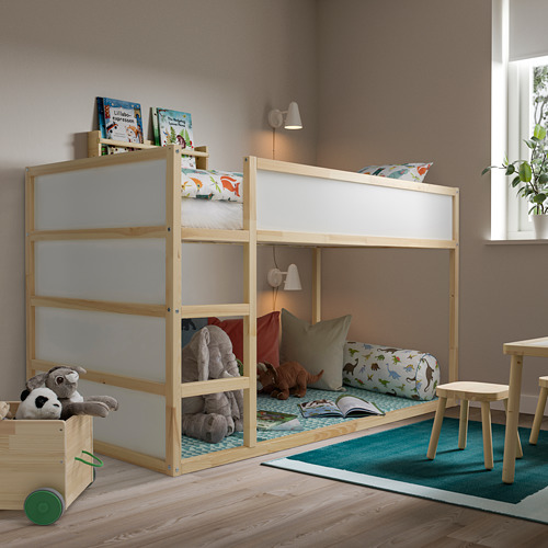 Habitación infantil con cama KURA, madera clara, peluches, almohadas de colores, alfombra azul y luz natural.