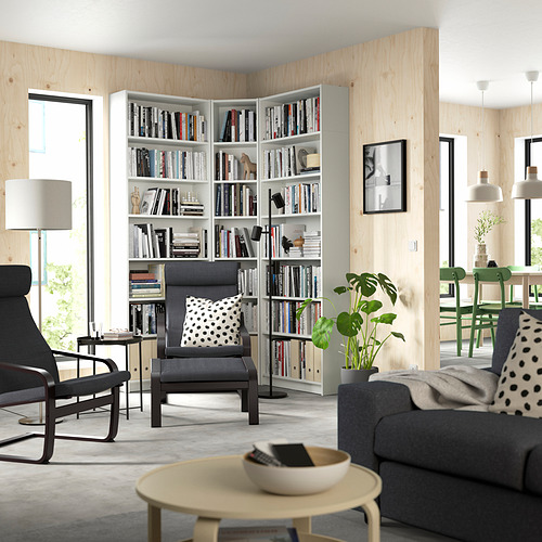 Sala de estar moderna con estantería blanca BILLY llena de libros. Muebles grises, grandes ventanales, plantas y decoración minimalista.