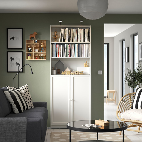Sala de estar moderna con estantería blanca BILLY contra pared verde, sofá gris oscuro, mesa de centro de vidrio y detalles en blanco y negro.